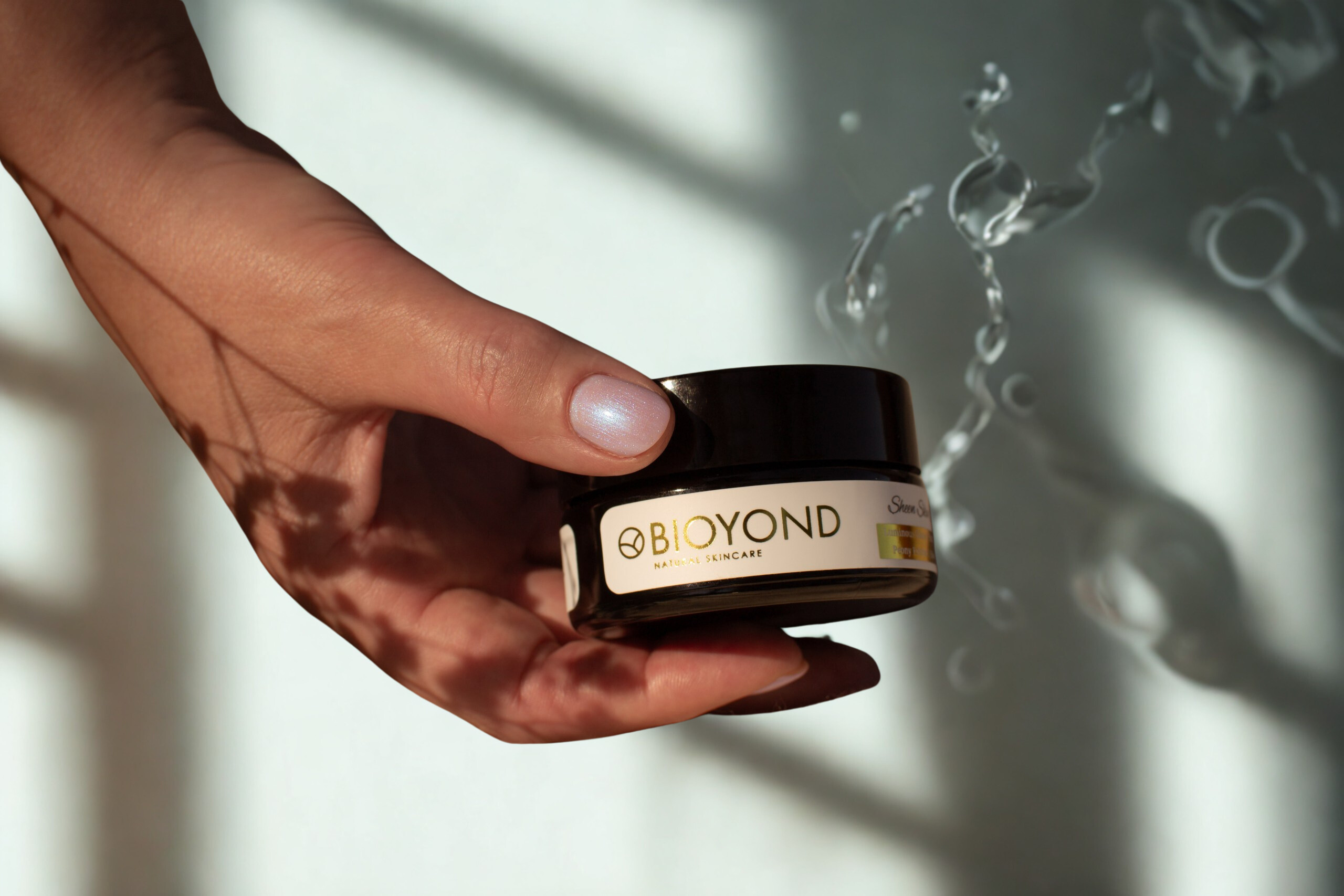Hands holding BIOYOND Sheen Skin Cream jar near water, symbolizing natural radiance and hydration for youthful skin